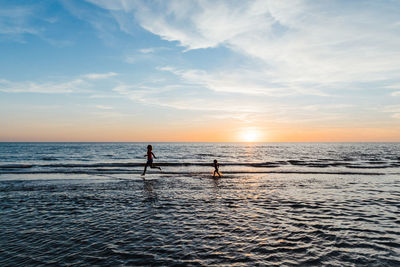 Silhouette people on sea against sky during sunset