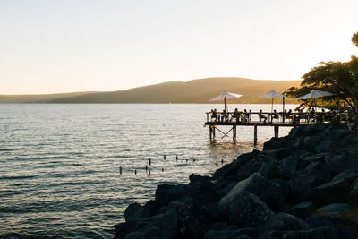 People in cafe on pier by lake against sky