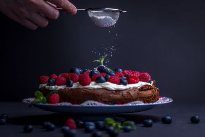 Cropped image of hand pouring powdered sugar into cake