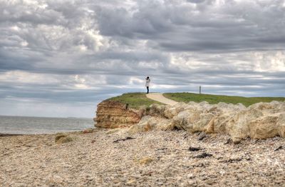 Man standing on footpath against cloudy sky