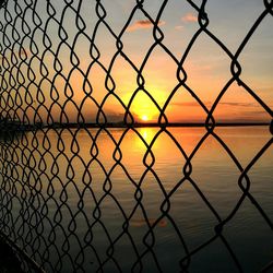 Close-up of chainlink fence against sky during sunset