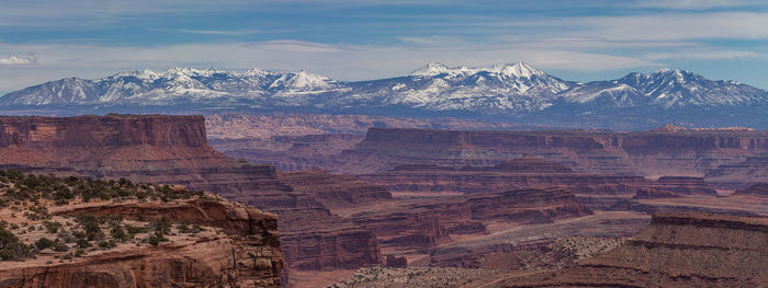 White snow-capped mountains beckon in the distance past rugged red sandstone rock cliffs and canyons