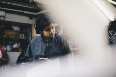 Female mechanic seen through open vehicle hood at auto repair shop