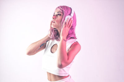 Woman with pink hair listening music against white background