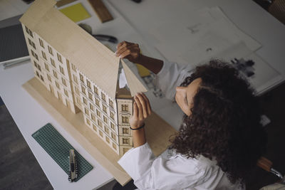 High angle view of female construction engineer preparing building model at desk in office