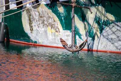 The anchor of a grungy boat hangs above water