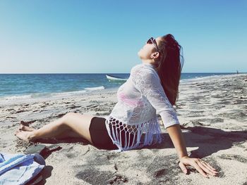 Young woman resting at beach against clear sky