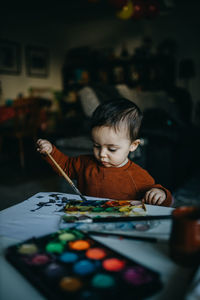 Baby boy with art and craft equipment on table at home