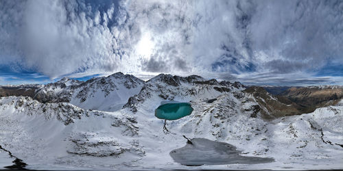 Panorama of mountain snow-covered range with turquoise lake, sunny day with clouds