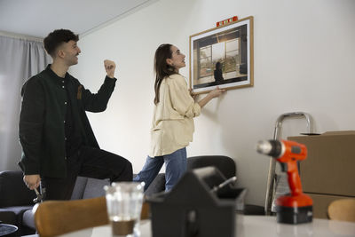Woman adjusting picture frame while boyfriend guiding her in living room