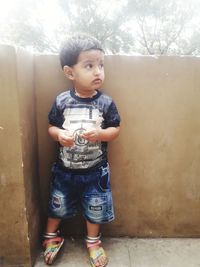 Boy looking away while standing against wall