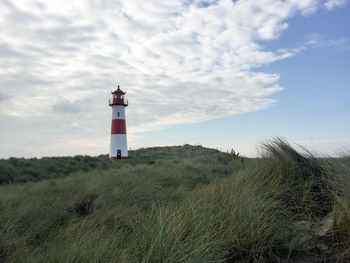 Lighthouse on grassy field against cloudy sky 