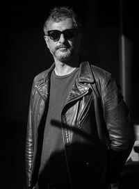 Portrait of young man wearing sunglasses standing against black background