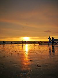 Silhouette people on beach against sky during sunset