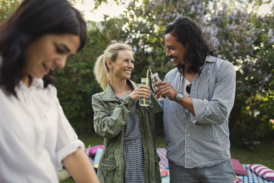 Happy couple toasting drink bottles during summer party in yard