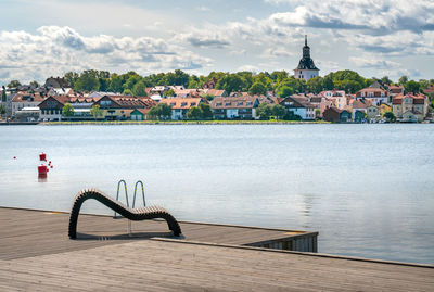 Pier over river by buildings in city against sky