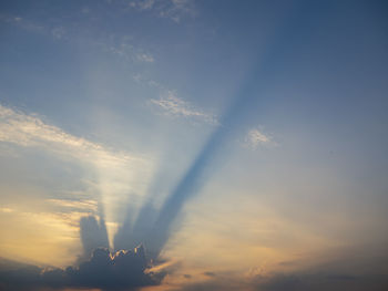 Low angle view of sunlight streaming through clouds during sunset