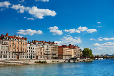 Buildings by river against blue sky