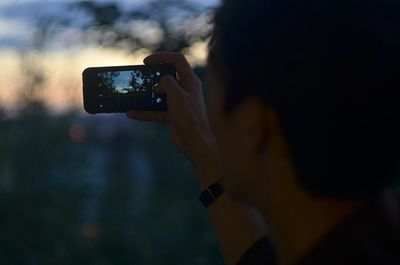 Midsection of person using mobile phone at sunset