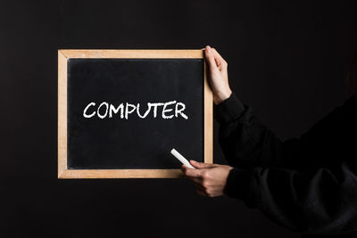 Midsection of man holding blackboard against black background