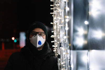 Portrait of young man wearing mask by christmas lights