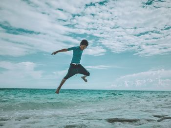 Full length of young man jumping in sea against cloudy sky