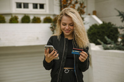 Smiling blond woman buying online through mobile phone and credit card