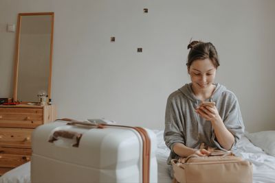 Woman with the baggage, smartphone and passport at home, preparing to flight