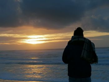 Rear view of woman looking at sea against sunset sky