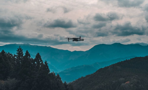 Low angle view of airplane flying over mountains against sky