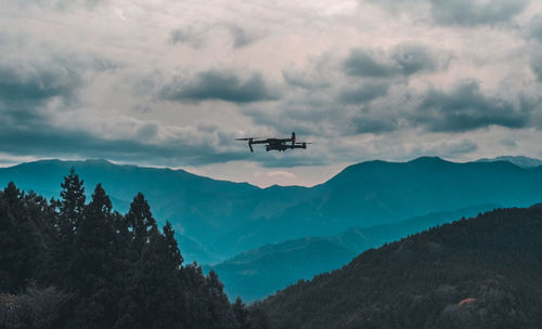 Low angle view of drone flying over mountains against sky