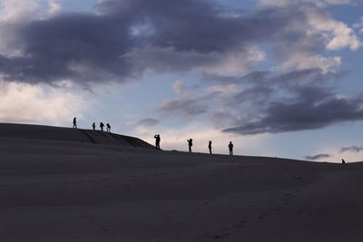 People on sand dune against sky