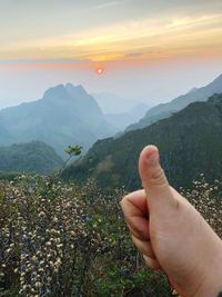 Cropped image of hand on mountain against sky during sunset