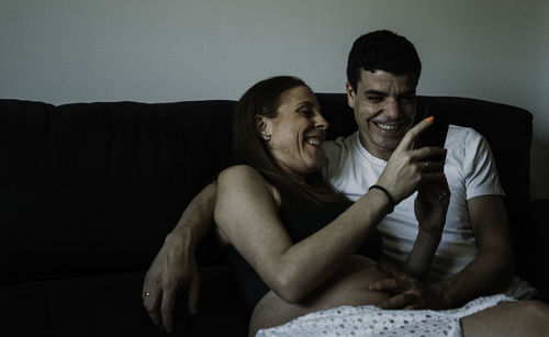 Pregnant woman using phone while sitting by man on sofa at home