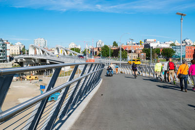 People on bridge in city against sky