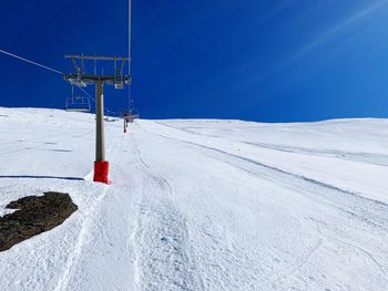 Low angle view of ski lift on snowcapped mountain against clear blue sky