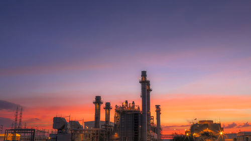 Illuminated factory against sky during sunset