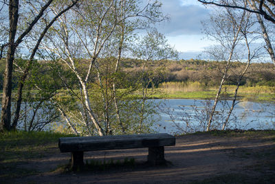 Bench in park by lake against sky