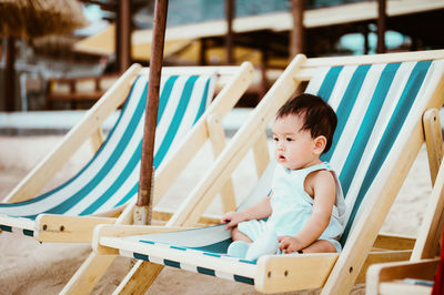 Cute baby boy sitting on chair at beach