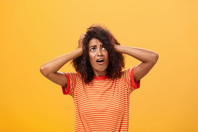 Portrait of young woman standing against yellow background