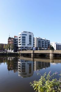 Buildings by river against clear blue sky