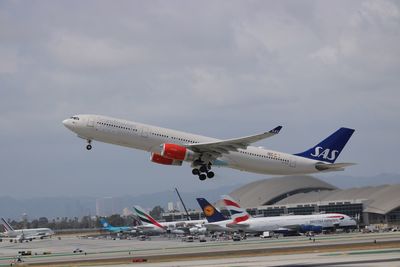 Airplane flying over airport runway against sky