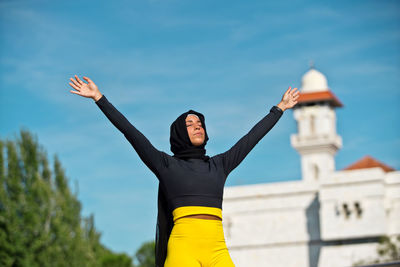 Woman with arms outstretched standing against sky