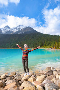 Full length of man standing on rock by lake against sky