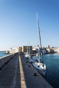 Sailboats moored at harbor against clear sky