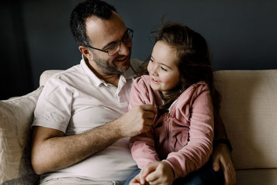 Smiling father looking at daughter while sitting on couch in living room