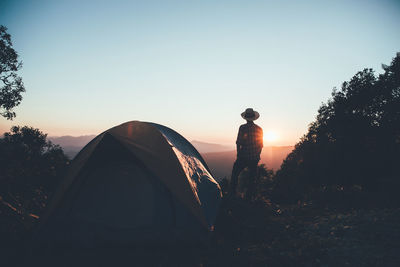 Rear view of man standing by tent on mountain against sky during sunrise