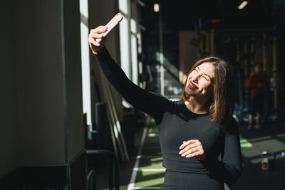 Portrait of resting young brunette woman in sport active wear taking selfie in fitness club