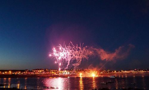 Firework display over illuminated city against sky at night