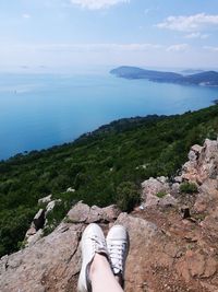 Low section of woman standing on cliff by sea against sky